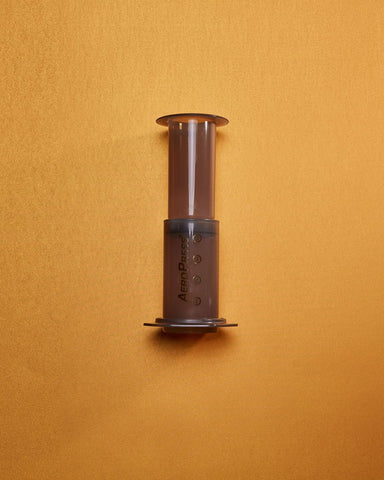 An Aeropress pictured laying on an orange background
