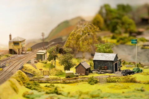 Model railroad buildings in a rural setting next to a track, with miniature trees
