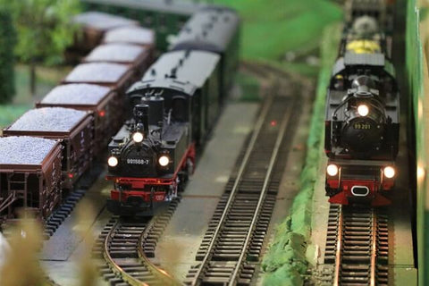 Black and red steam locomotive models sit at rest next to each other at a station