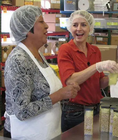 2 women with hairnets smiling and laughing while packing chili mixes do good shop partner