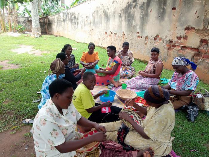 women weaving on grass under a mango tree in uganda, africa