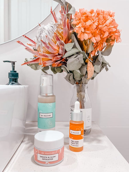 Image of Be three Fraiche skincare products cleanser, face oil, face scrub on top a bathroom sink with organge dry flowers