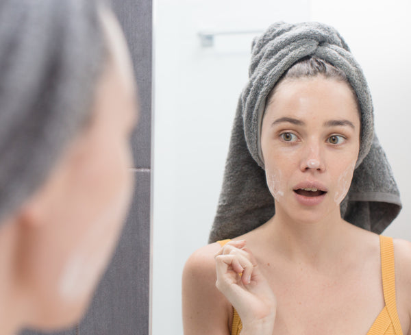 Young woman with Be Fraiche Tea Cleanser on her face looking at the mirror