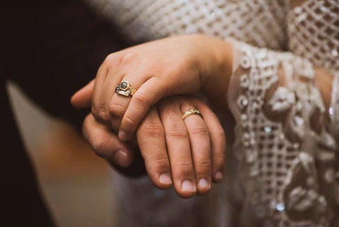 Two clasped hands, wearing gold wedding rings