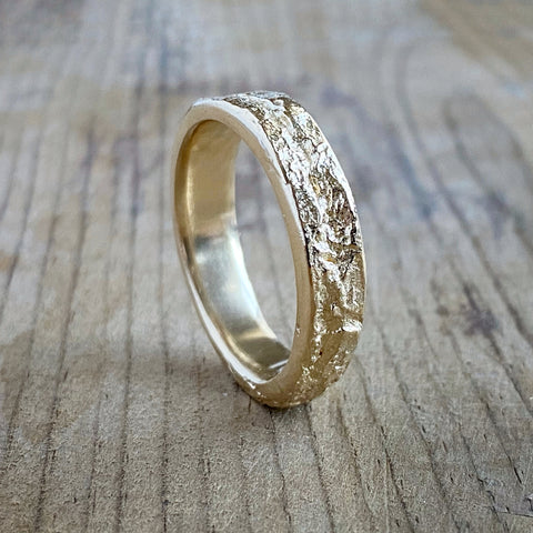 Large textured gold ring standing on its edge, resting on a rustic wood background