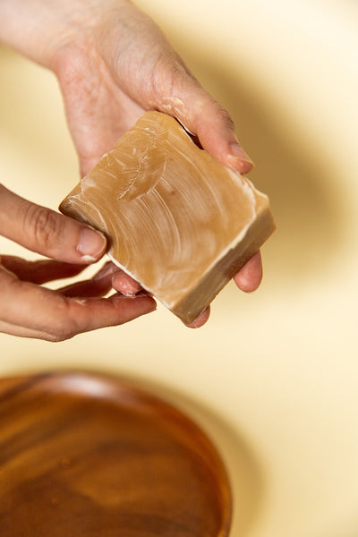 An image of hands holding an ochre colored bar of soap