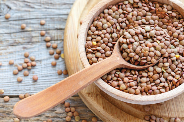 Image of a wooden bowl full of lentils with a wooden spoon on a painted wood table