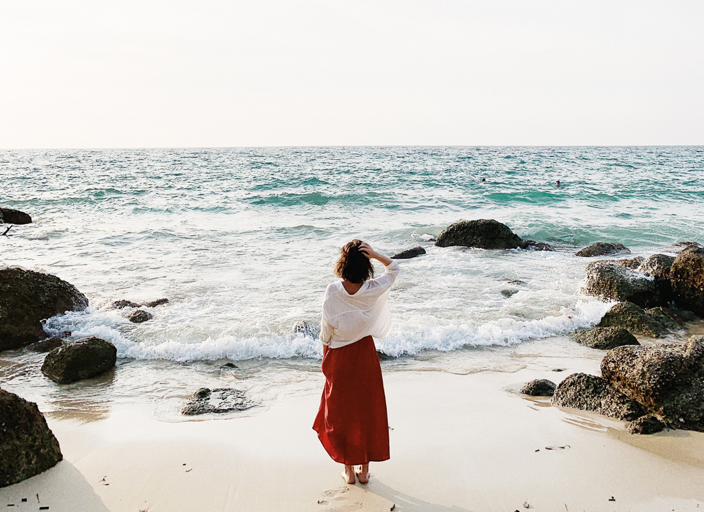 woman stands at the edge of the sea shore looking out over the ocean