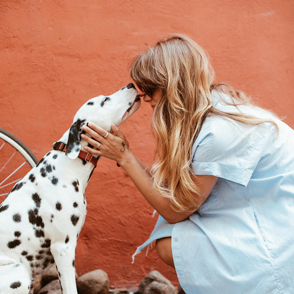woman bends down to kiss dog in front of an orange wall