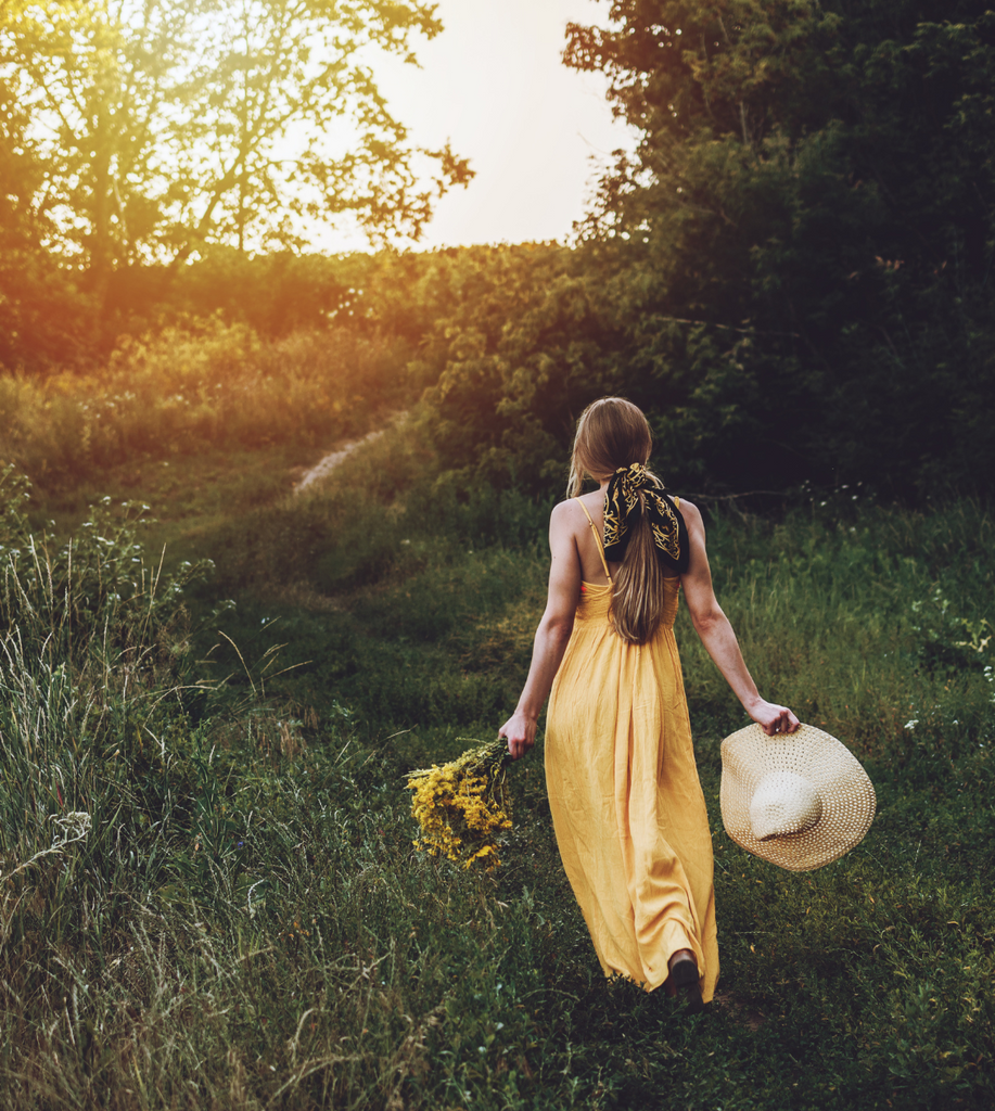 woman walks toward the setting sun in a green grassy field