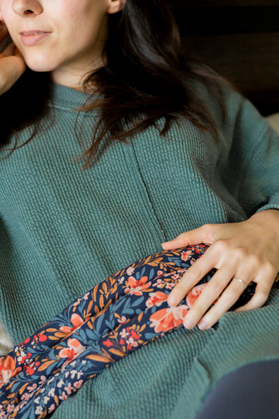 Image of a woman in a green sweater holding a Slow North heated neck wrap across her stomach