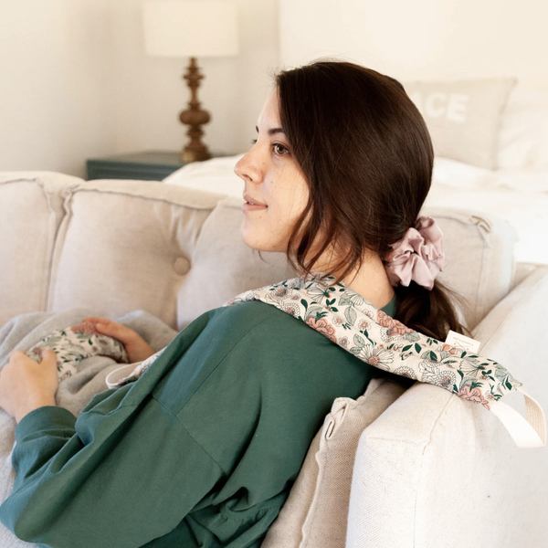 An image of a woman sitting on a couch with a Slow North heated neck wrap draped over her shoulder