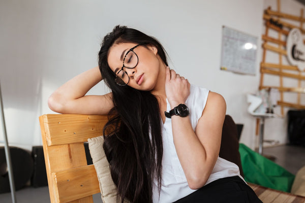 An image of a woman with neck pain sitting on a chair in a home office