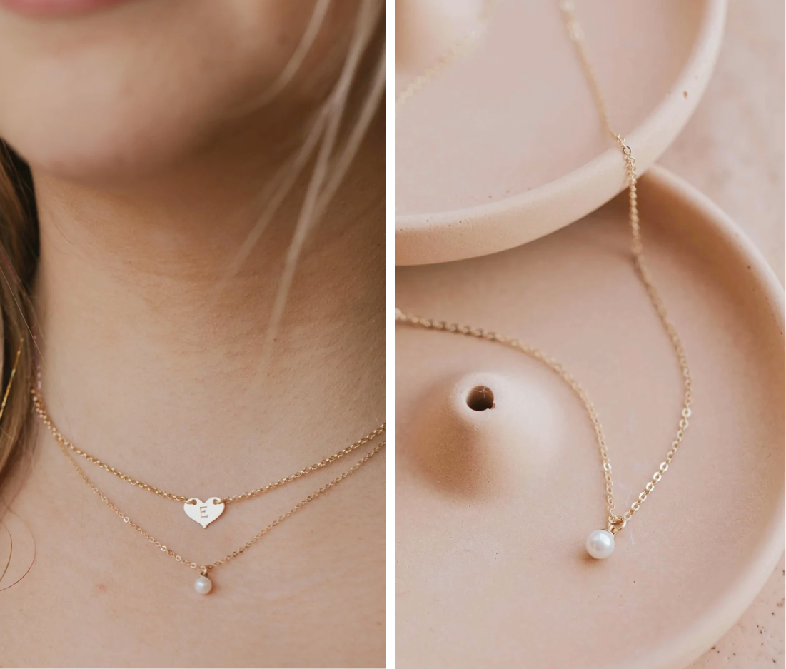 A pearl necklace layered with a heart pendant necklace that is hand stamped to create an initial necklace by Hello Adorn.