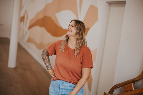 Jess standing in front of mural in terracotta shirt.