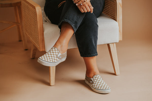 Checkered vans and black jeans on Jess sitting in chair. 