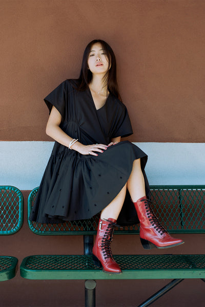 Sarah Kinsley on a green bench and leaning against an orange wall wearing Merlette BALLOU DRESS