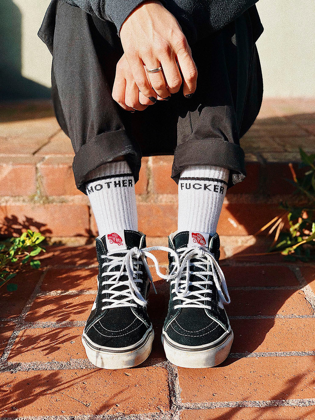 Sitting on step with arms crossed wearing vans high tops and mother fucker socks