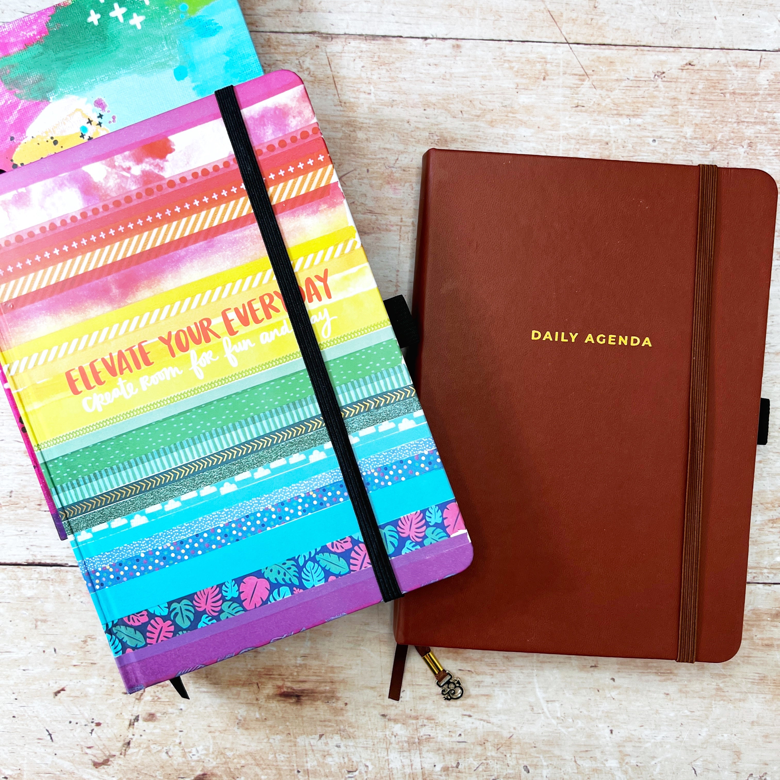 Bright coloured planner with ‘ elevate your everyday’ written on it and a brown planner