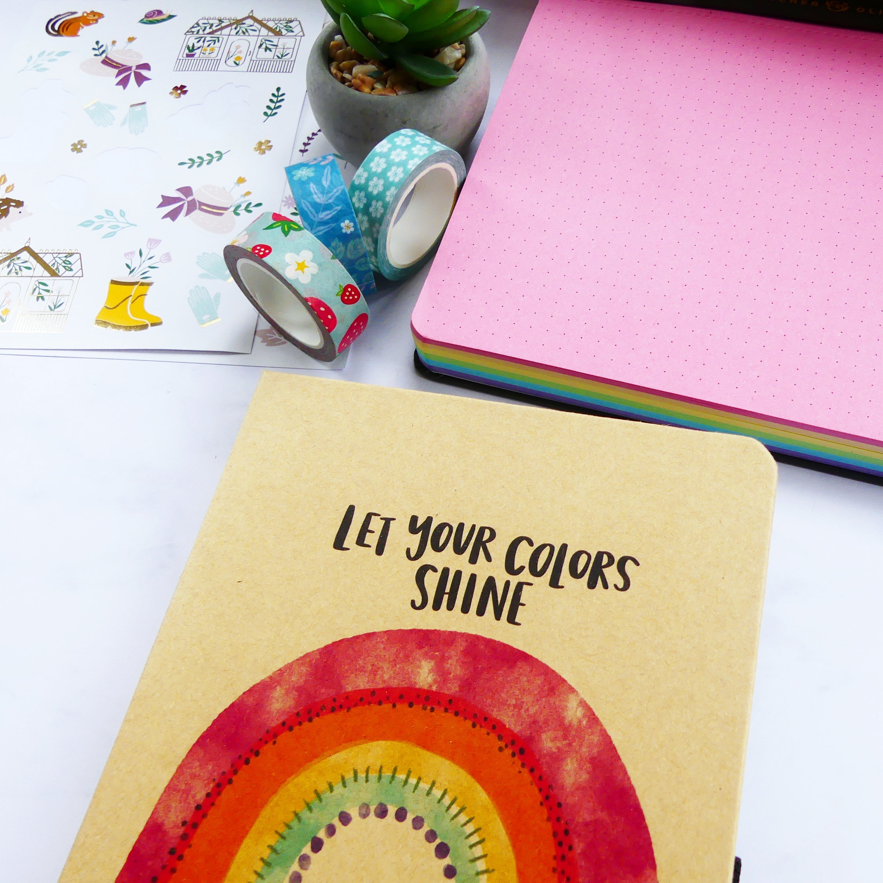 Image of journal with a rain bow and let your colours shine text, 2 coloured notepads below