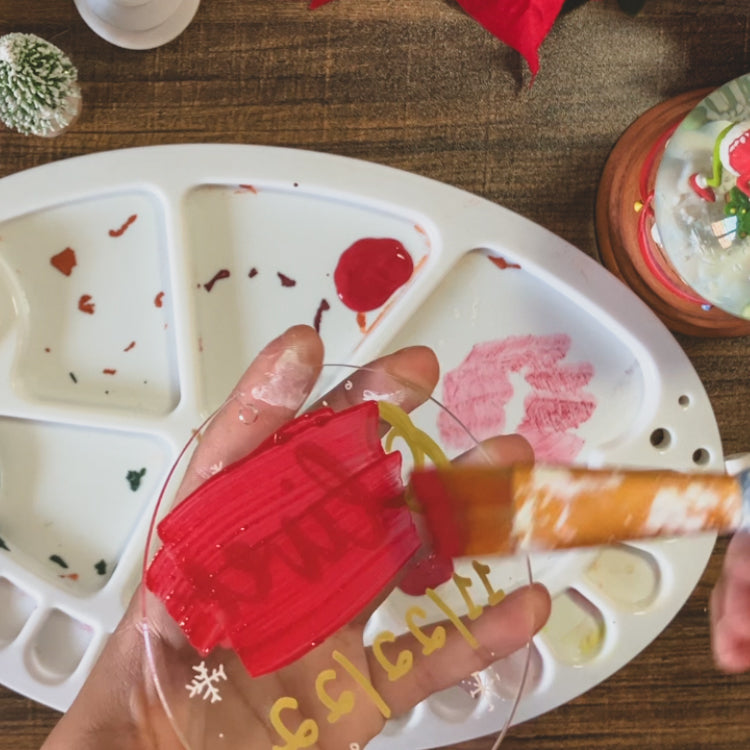 Emily is painting the back of an clear, acrylic ornament red.