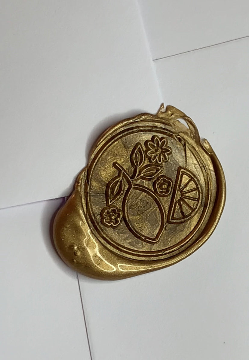 close up of a bronze wax seal featuring a lemon and floral design on an envelope 