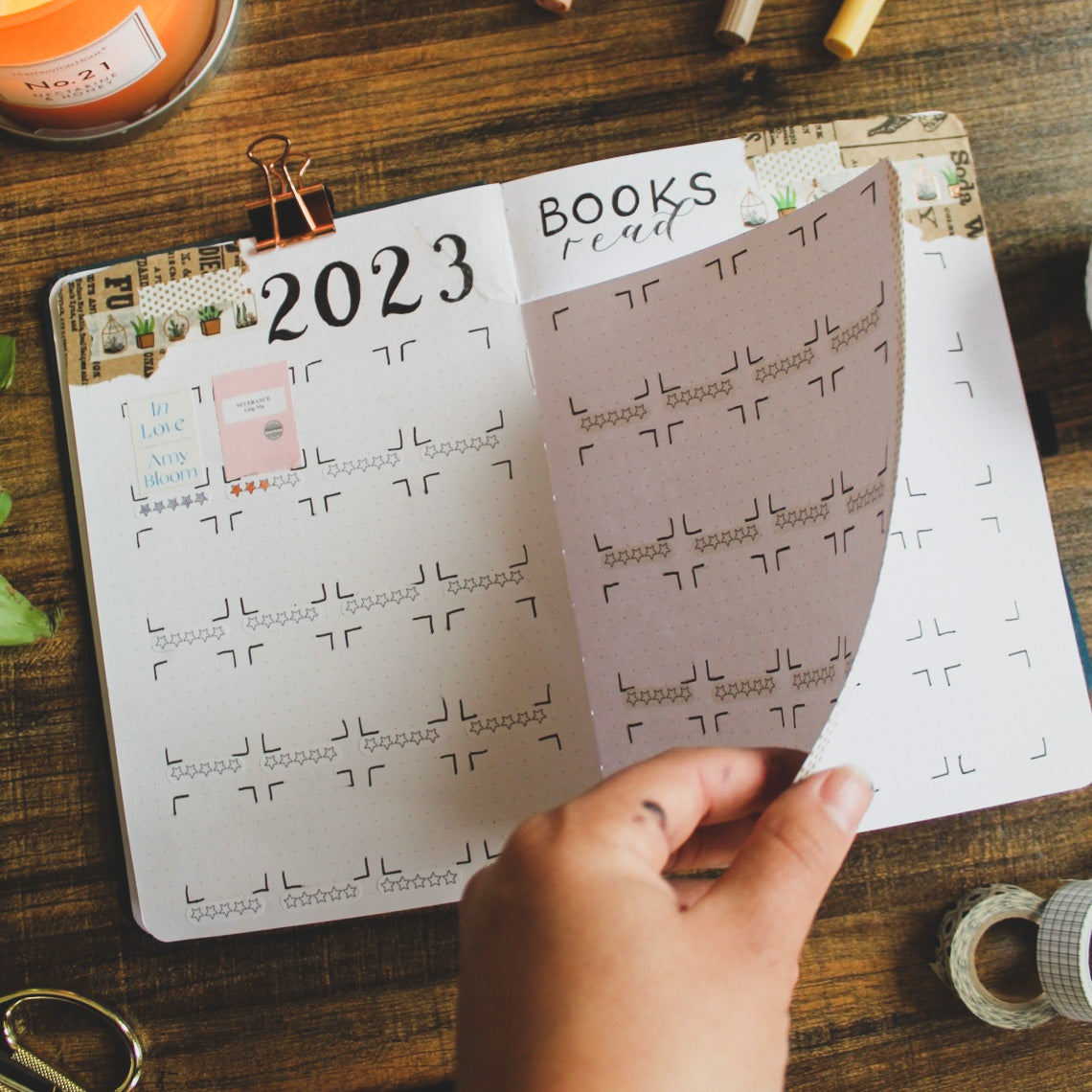 A notebook with white pages is open, lying on a dark surface. The journal has a dutch door page and has boxes for small book cover photos titled 2023 Books Read.