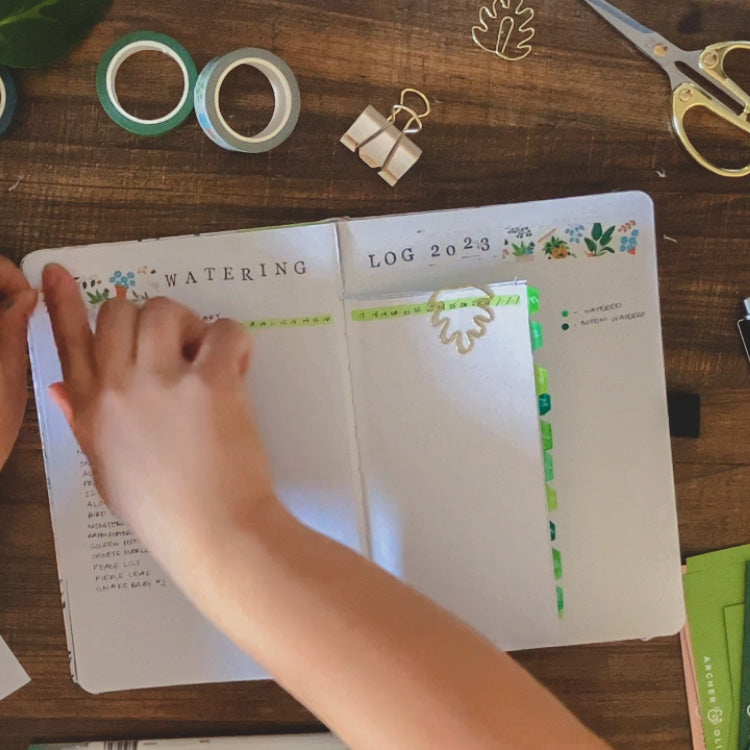 Emily is adding some plant washi tape to her watering tracker in her plant journal. 