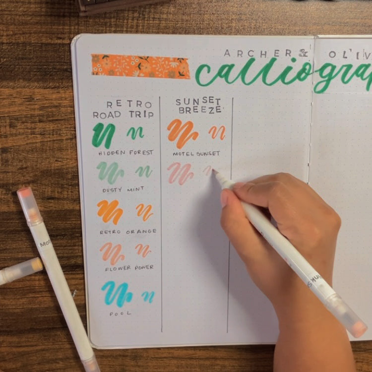 Emily is swatching her calliograph pens into a notebook titled "Archer and Olive Calliographs"