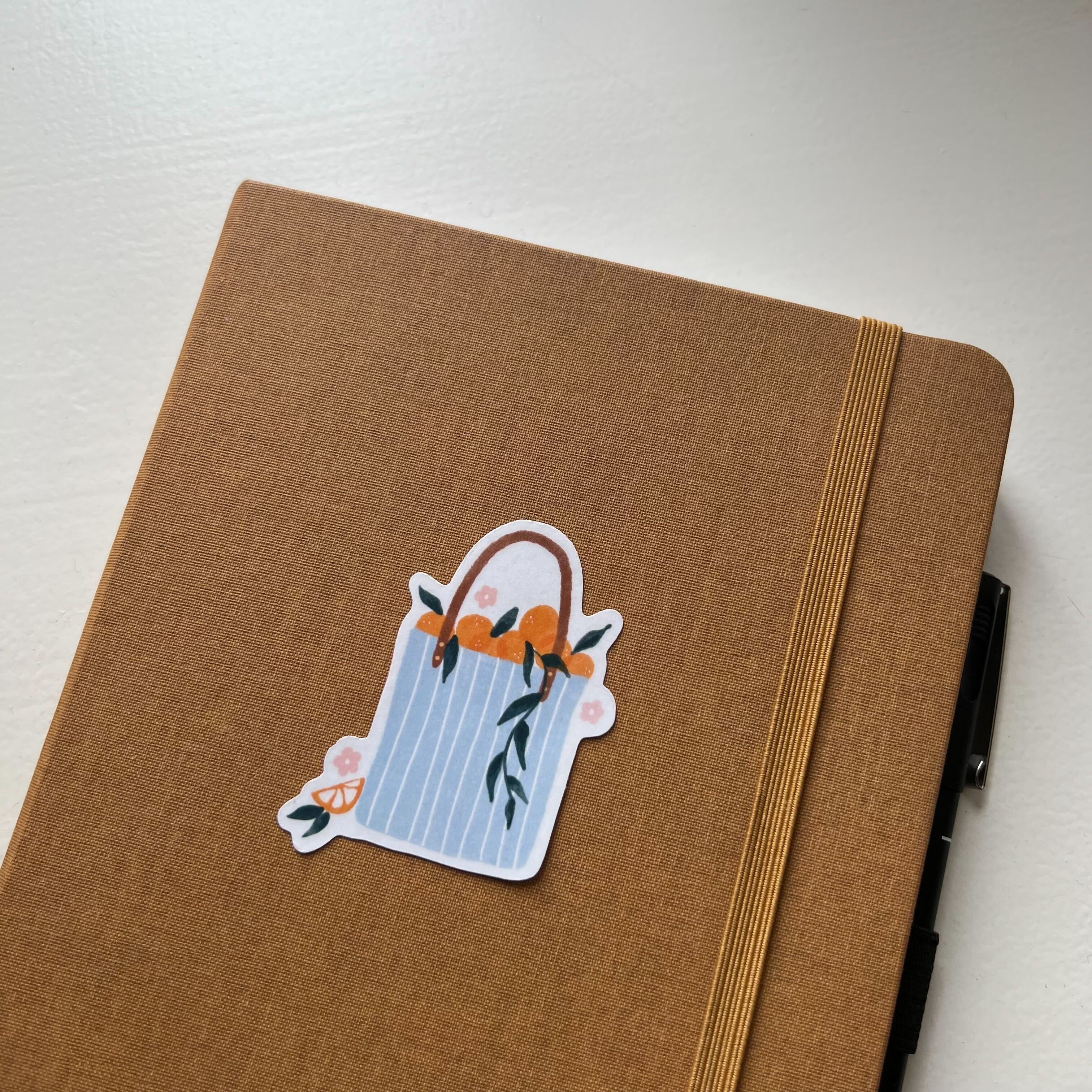 a sticker depicting a summer tote bag full of oranges on a brown notebook