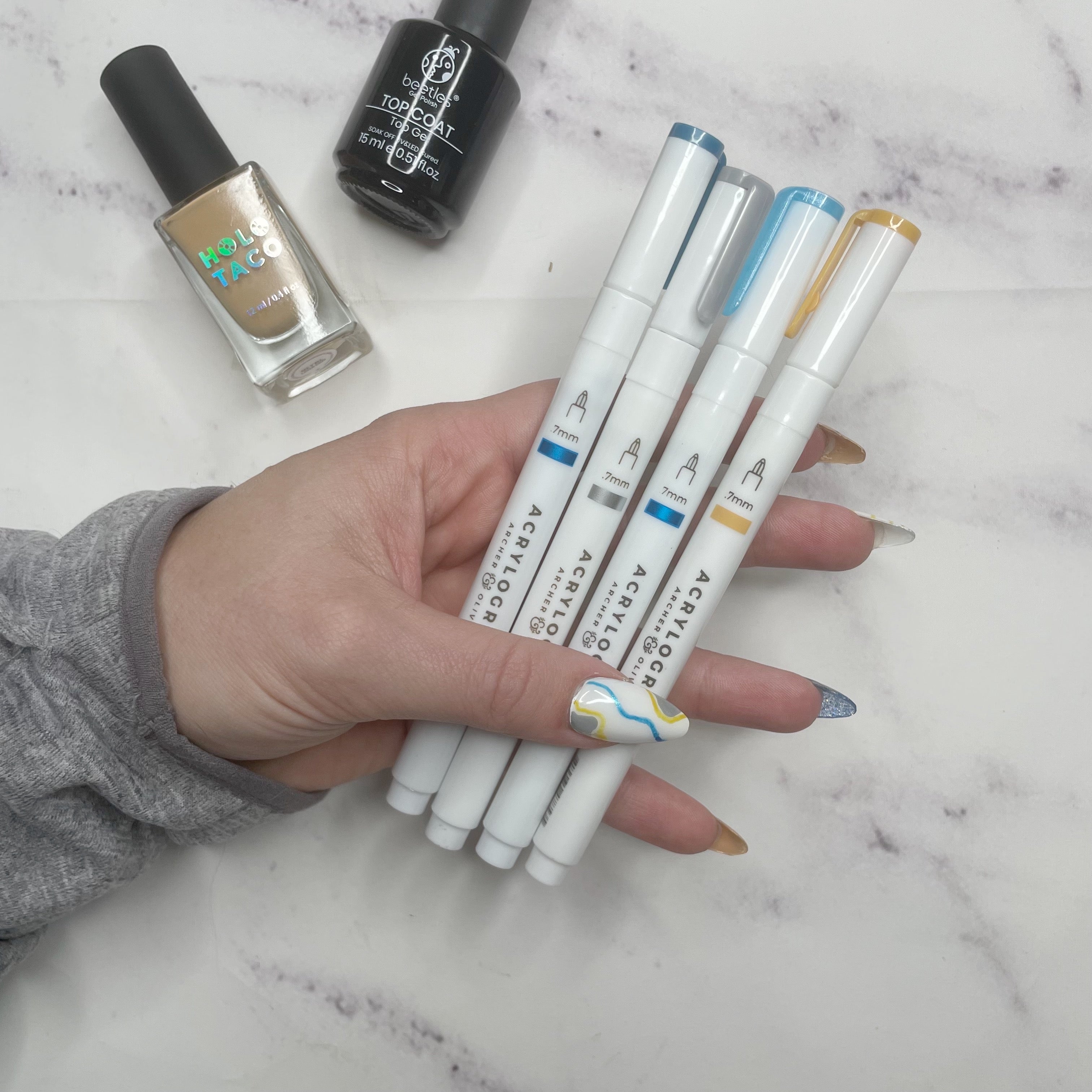 Acrylogrpah pens used on nails including silver metallic, blue metallic, blue glitter, and golden hour