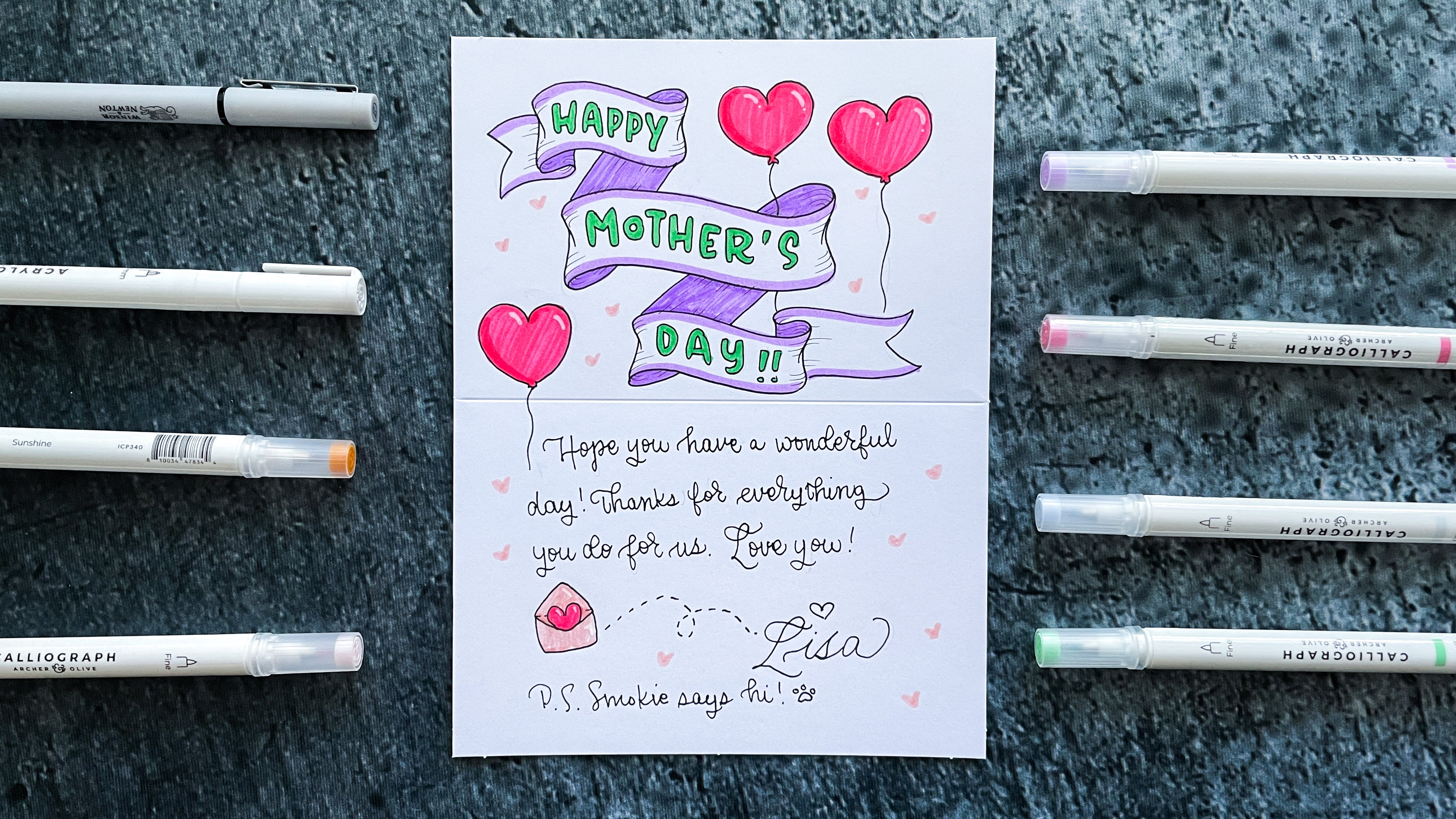 text of happy mother's day with message surrounded by heart doodles on cardstock surrounded by pens
