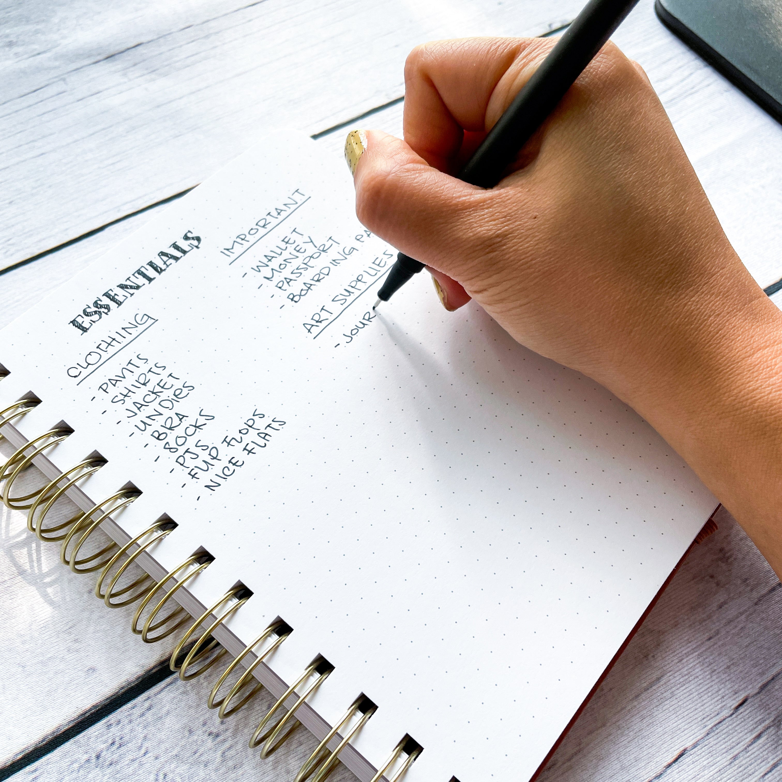 image of hand holding a pen writing travel packing list on spiral bound journal