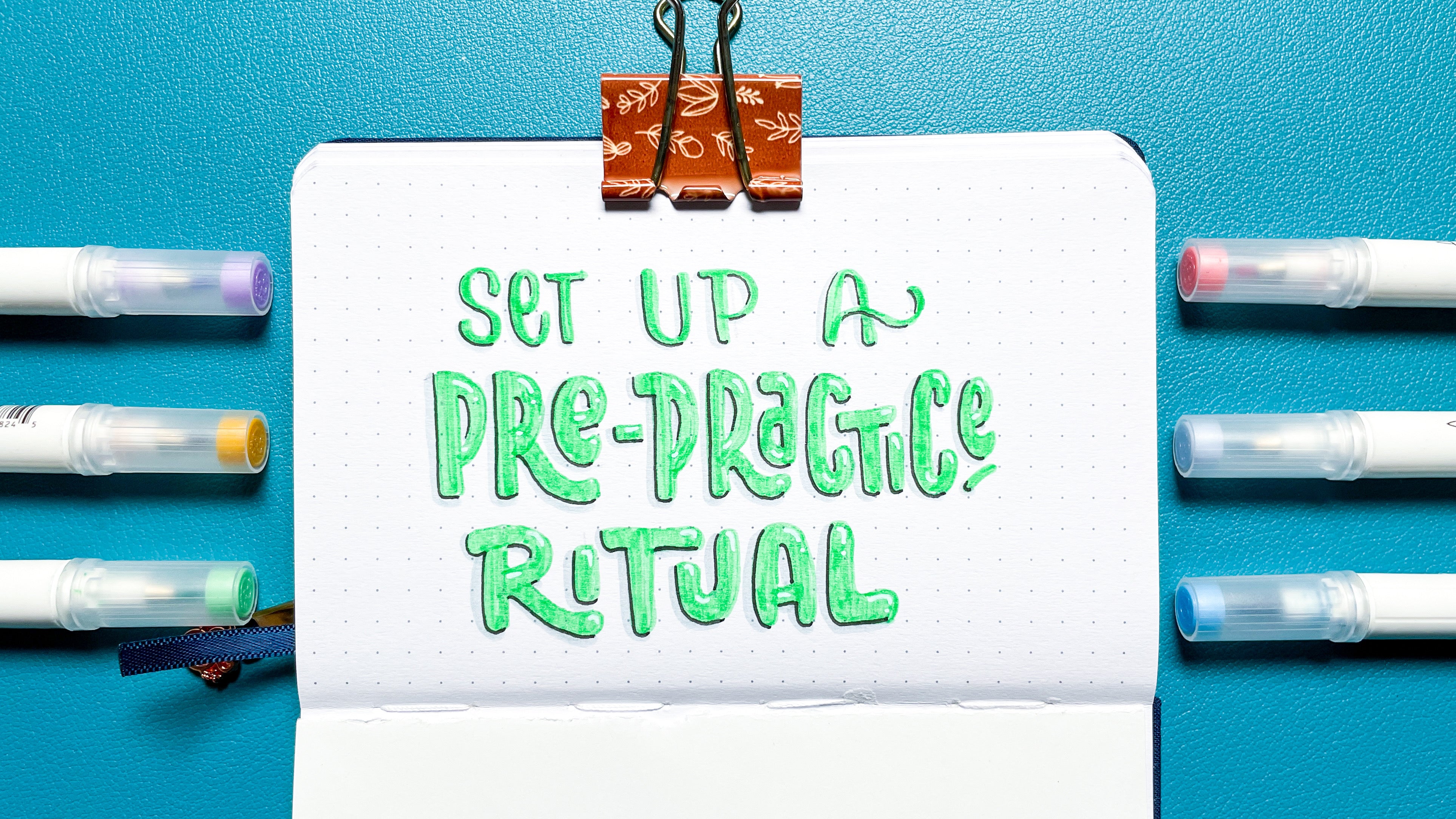 image of hand lettered "setup a pre-practice ritual" in a dot grid journal surrounded by A&O Calliographs