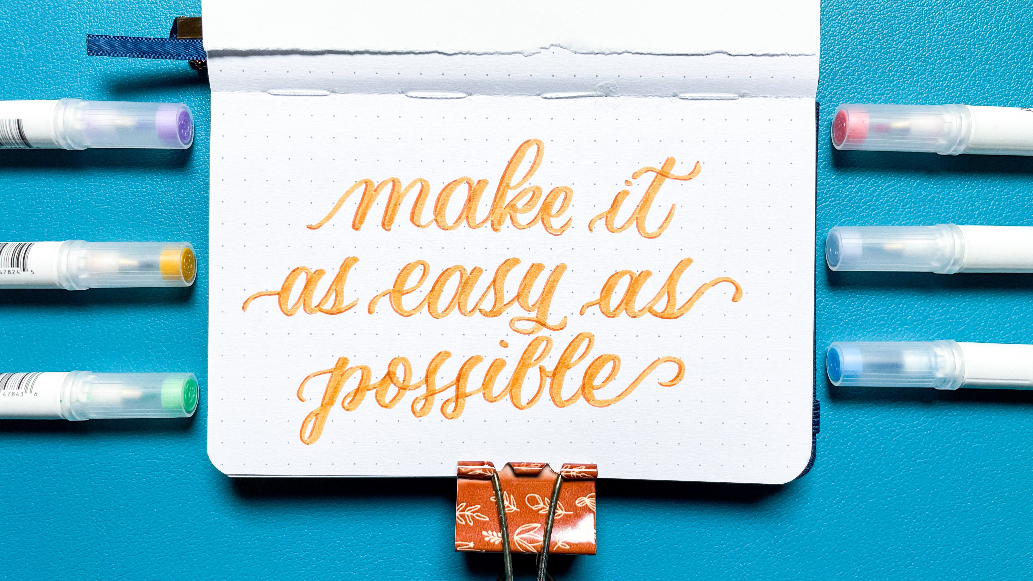 image of hand lettered "make it as easy as possible" in a dot grid journal surrounded by A&O Calliographs