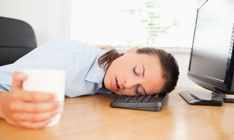 Woman sleeping in the office while holding a cup of single serve coffee