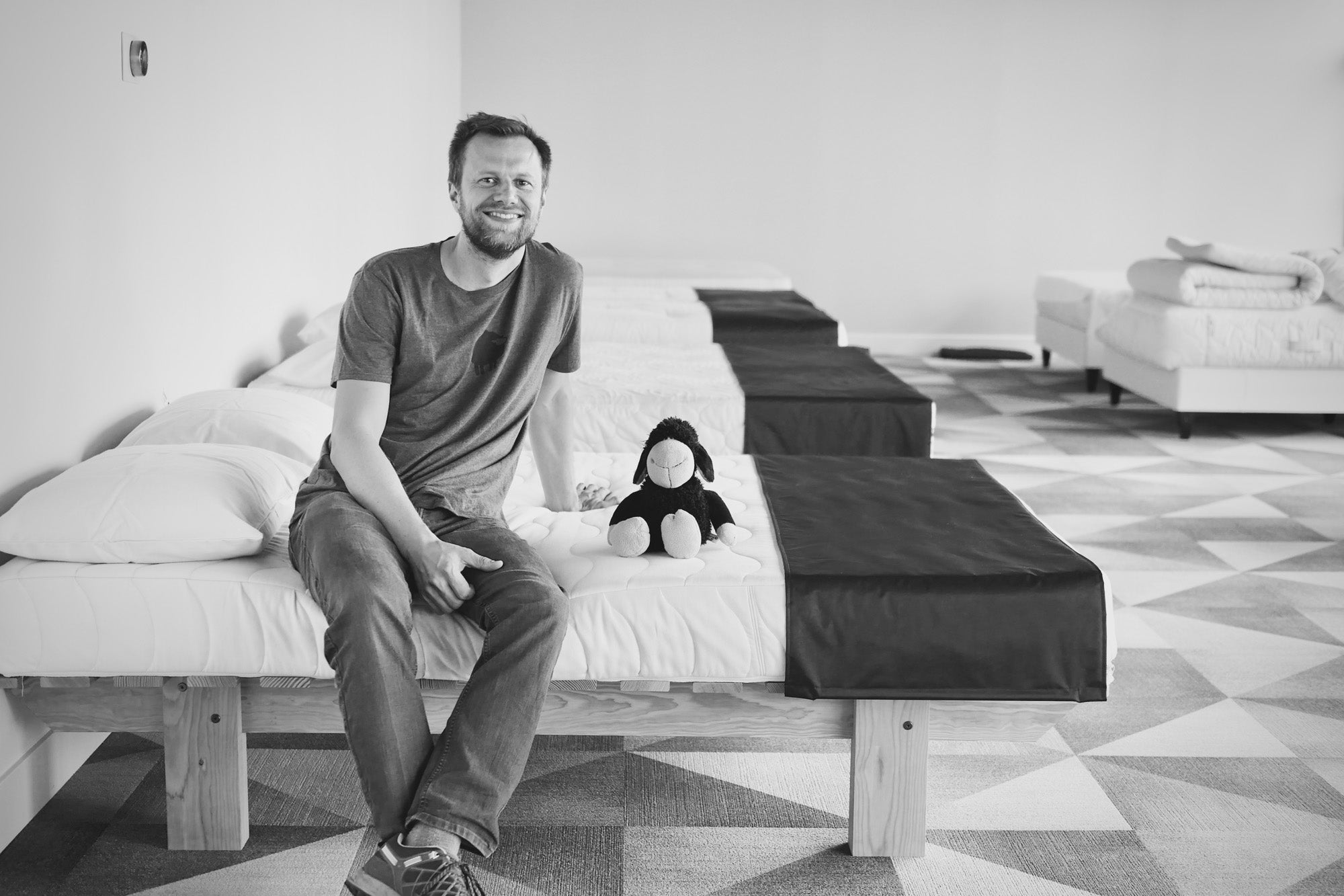 Christian Schmidt, owner of Black Sheep Mattress Company, sitting on a mattress with a sheep toy beside him