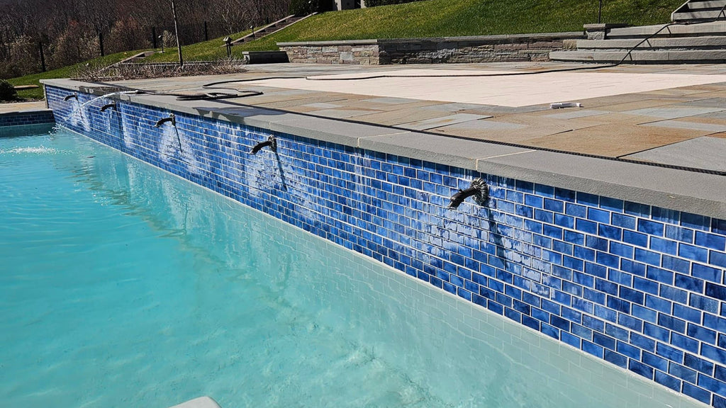a blue tiled pool wall with scuppers that's suffering from severe efflorescence damage.