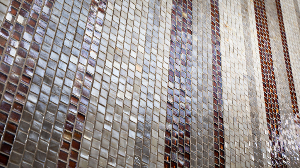 An angled shot of tile from Murrine Mosaics in light cream and amber installed in a shower wall.