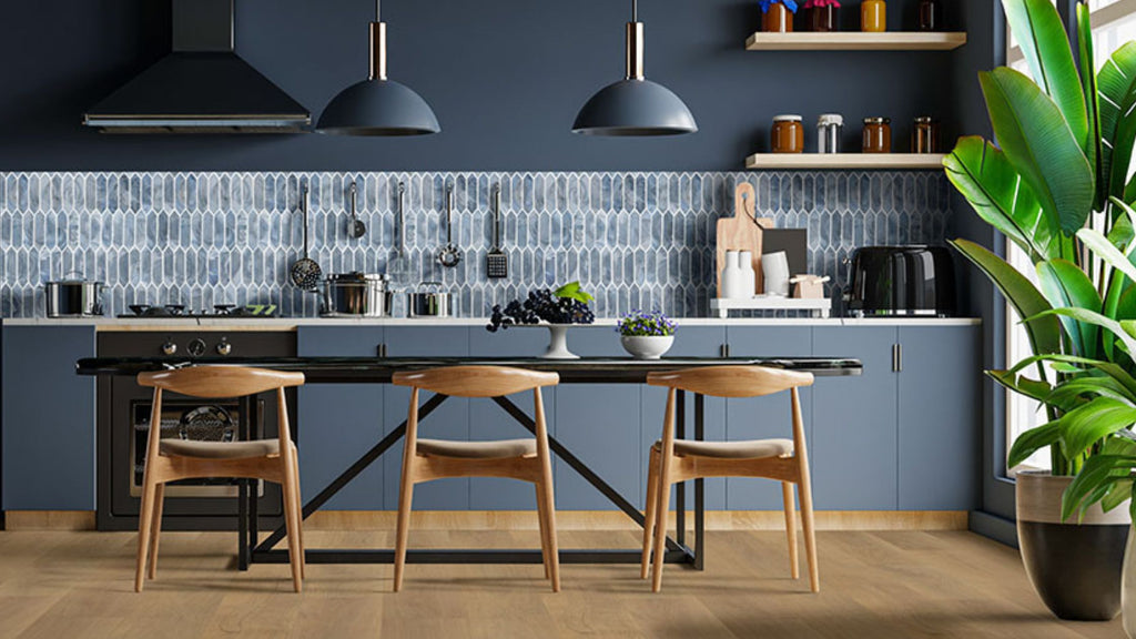 Blue picket tile backsplash in a modern kitchen with blue cabinets and light oak wood floors and chairs. There's a green plant on the right of the image.