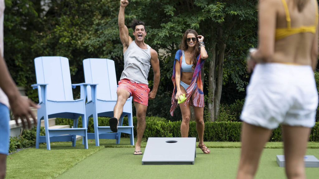 A man and woman playing cornhole. The man is jumping in the air and yelling in celebration.