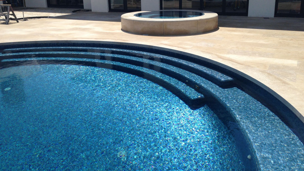 A luxury pool in the backyard of a modern home. It's tiled completely in the Blue Moon 1" x 1" glass tile by Vidrepur.
