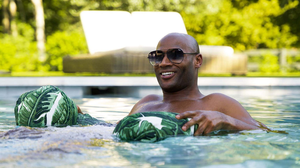 A man floating in a pool using a Laze Hammock with a tropical leaf pattern.