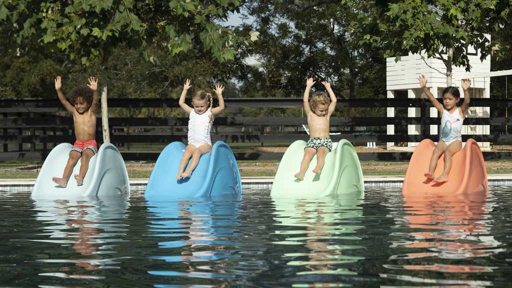 Four small children sliding down Ledge Lounger slides set up on a pool shelf.