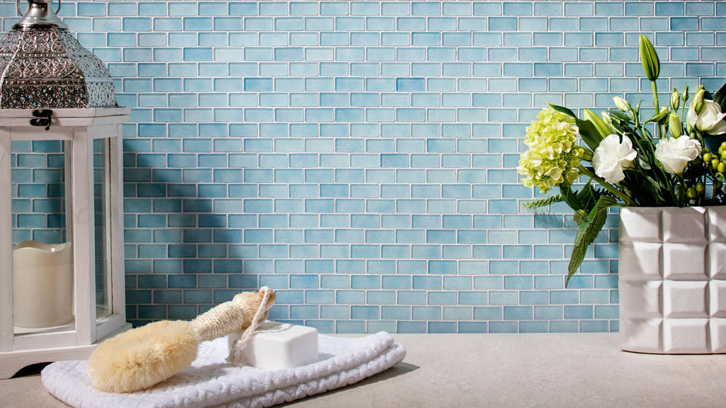 Light blue tile from the Quartz collection in the elongated shape. It's on the wall of a bathroom. There is white decor as well as a white pot with green and white flowers. A towel sits on the counter with a bar of soap and loofah on top.
