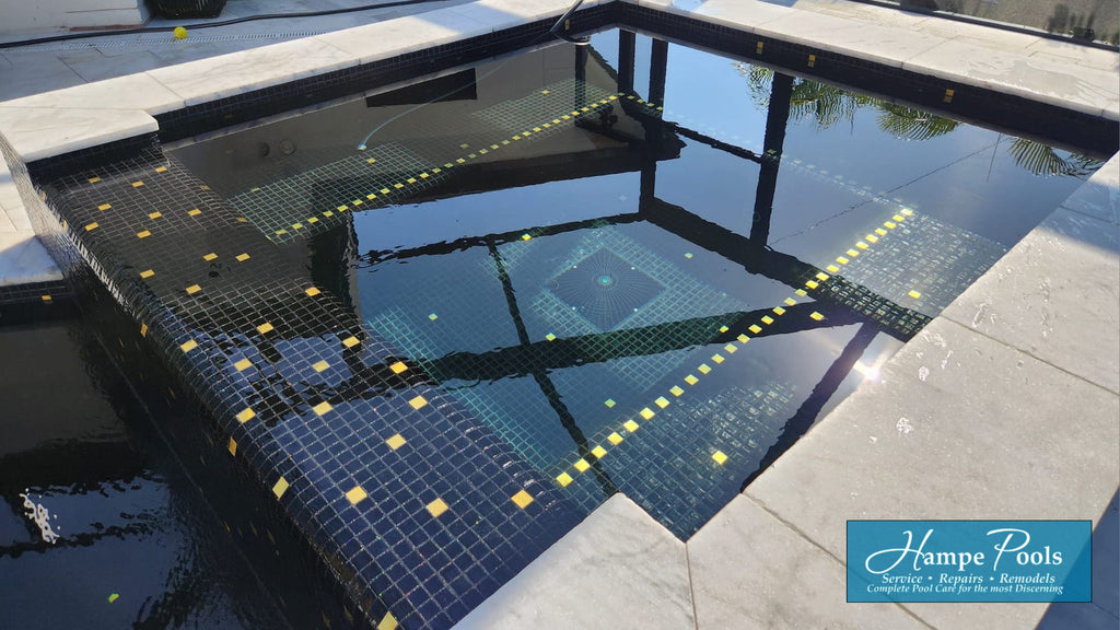 close up of a spa that runs into a pool finished in black glass and 24k gold tiles.