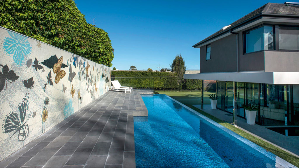 Glass mosaic butterfly mural wall around a luxury pool in the backyard of a modern home.