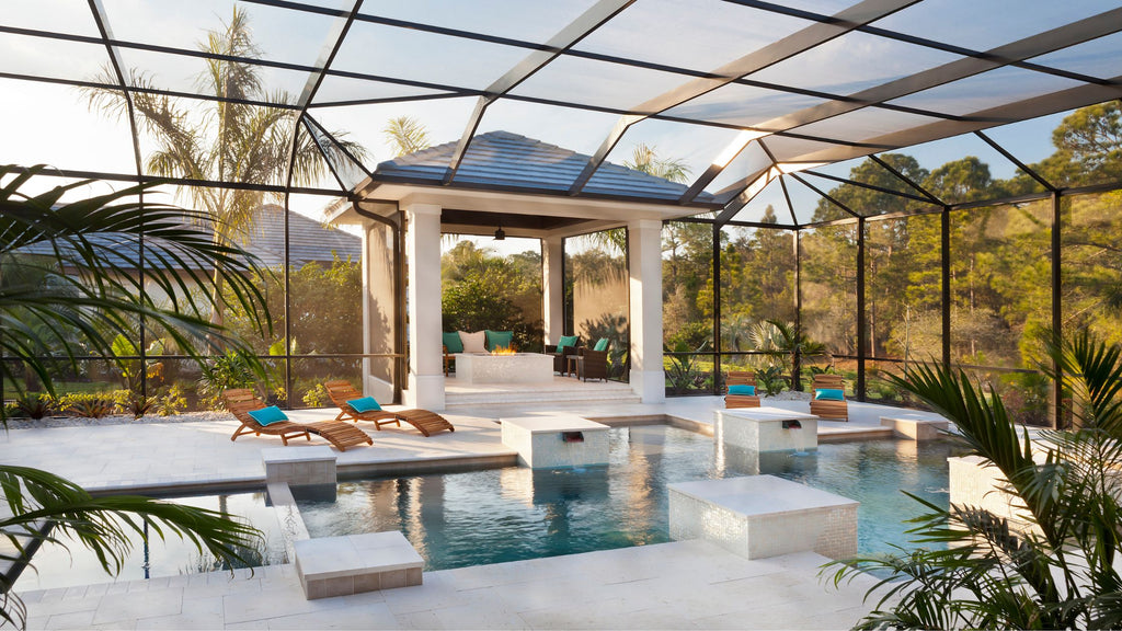 A beautiful, modern pool with a luxurious sitting area under a gazeebo looking out towards it. The pool is tiled with shiny, white tile which allows the blue decor and the lush greenery around to contrast with it beautifully.