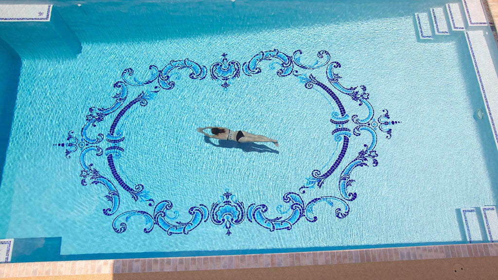 a large filigree swimming pool centerpiece in a large luxury pool. A woman in swimming across the pool.