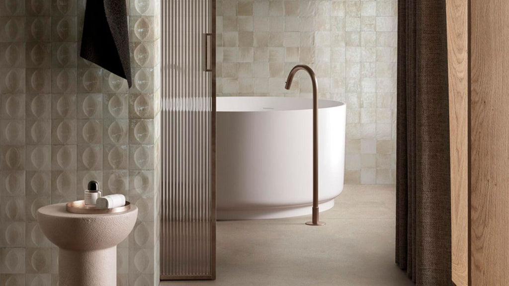 Beautiful, coordinating square tiles in a bathroom. One wall behind the bathtub sports a soft pastel pink and cream color tile while the wall behind the sink features matching tile with an egg shape texture running across the face of the tile vertically.